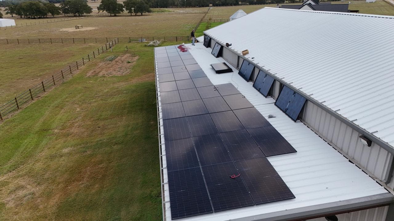 Crew installing solar panels on a white metal barn roof — Central Texas ranch